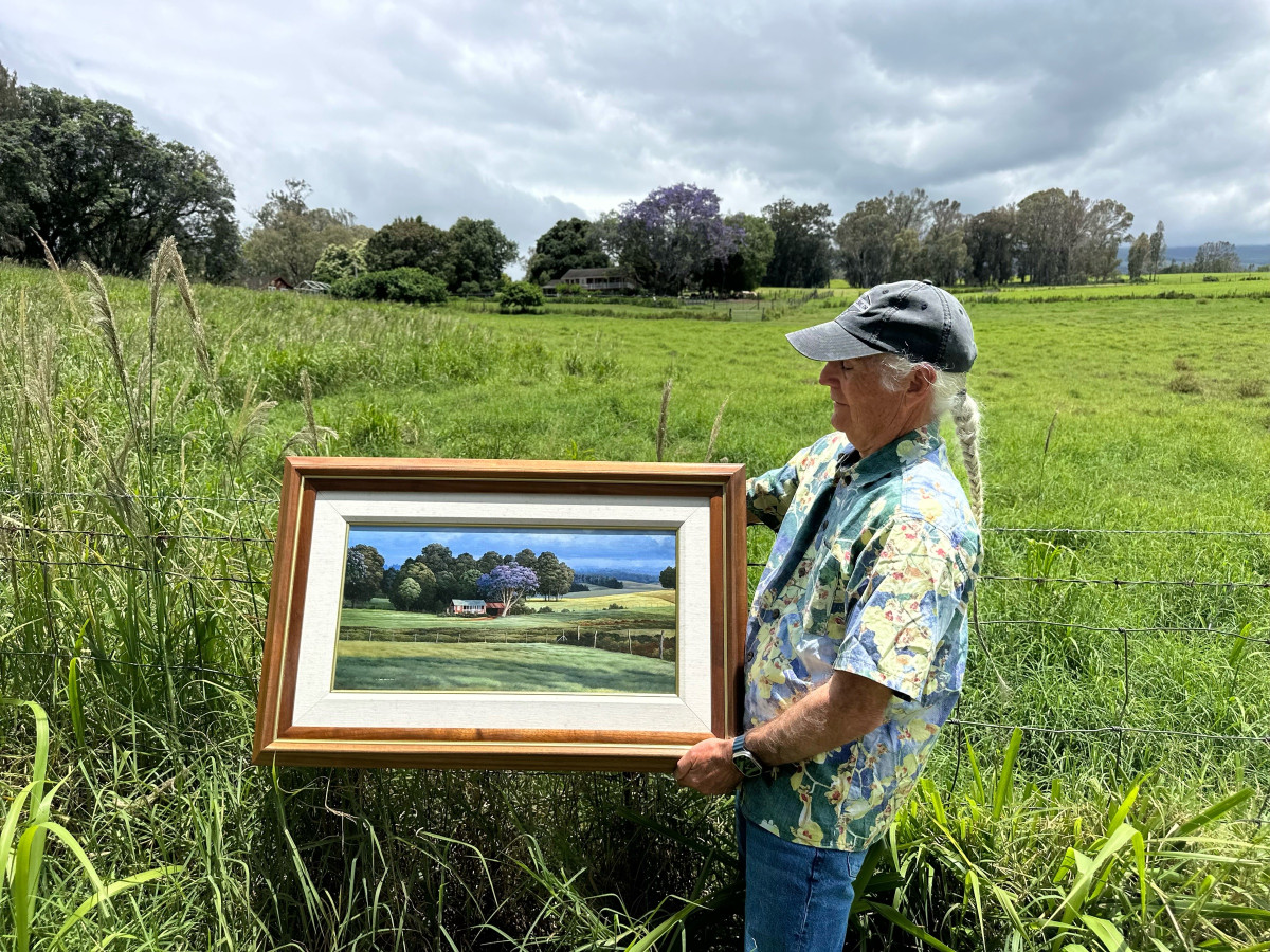A framed painting of the jacaranda and the house, held up beside a fence in front of the pasture it shows